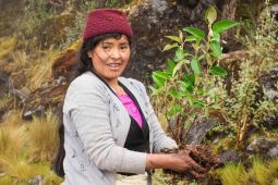 Woman holds plant while standing in grassy habitat.